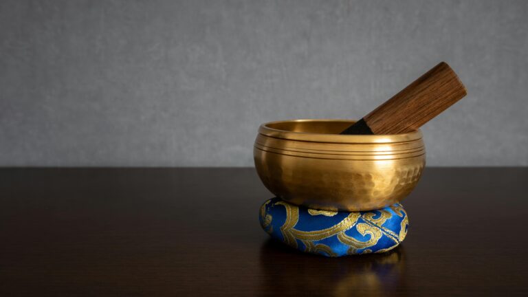 A golden Tibetan singing bowl on ornate blue cushion, perfect for meditation.