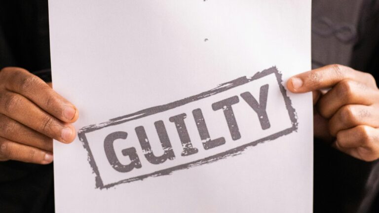 A close-up of a judge holding a document with a 'Guilty' verdict in a courtroom setting.