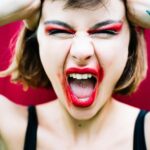 A woman with bold red makeup expressing intense emotion by shouting.