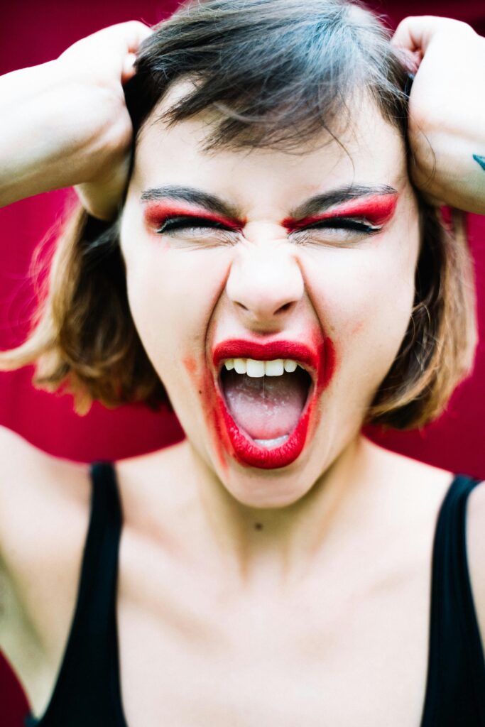 A woman with bold red makeup expressing intense emotion by shouting.