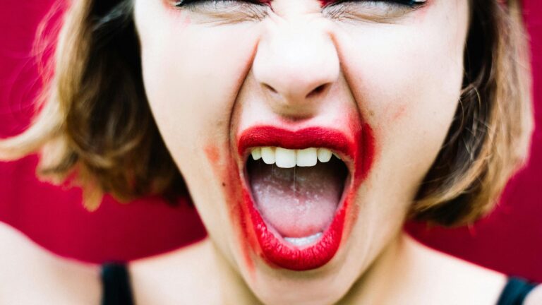 A woman with bold red makeup expressing intense emotion by shouting.